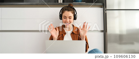 Portrait of happy young woman, freelancer working from home, remote worker sits on floor with laptop and headphones, looks surprised and excited at screen Portrait of happy young woman, freelancer working from home, remote worker sits on floor with laptop and headphones, looks surprised and excited at screen 109606130