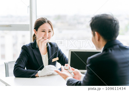 腕時計を質屋・リサイクルショップに買取査定に出すビジネスマンと鑑定士・査定士の女性 109611434