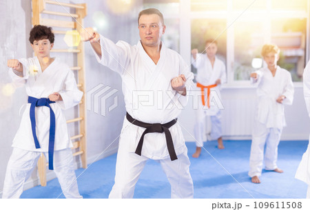 Karate kids in kimono performing kata moves with their teacher in foreground in gym during group training Karate kids in kimono performing kata moves with their teacher in foreground in gym during group training 109611508
