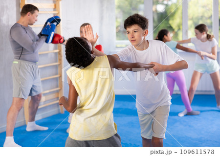 Two preteen boys learn to do power grabs in pairs during a self-defense lesson under the guidance of trainer in the gym 109611578