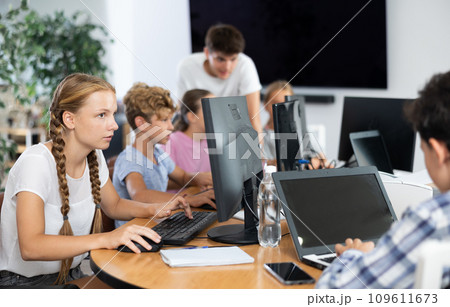 Portrait of teen schoolgirl sitting at table in computer class during lesson, smiling at camera. Concept of teenagers and technologies Portrait of teen schoolgirl sitting at table in computer class during lesson, smiling at camera. Concept of teenagers and technologies 109611673