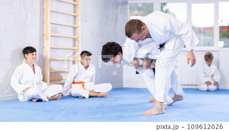 Skilled judo trainer demonstrating wrestling technique on juvenile practitioner 109612026