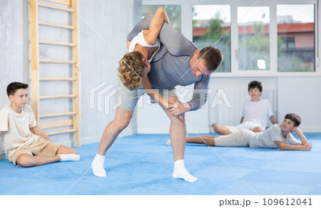 Skilled trainer demonstrating self-defense technique on juvenile practitioner 109612041