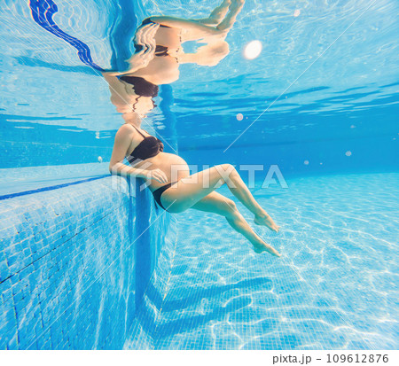 Embracing aquatic fitness, a pregnant woman demonstrates strength and serenity in underwater aerobics, creating a serene and empowering image in the pool 109612876