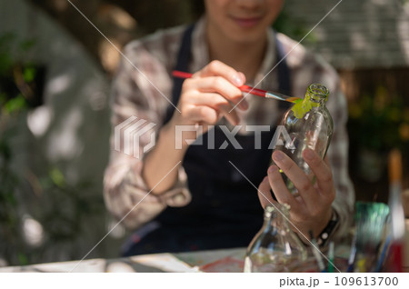 A positive and handsome young Asian man is handcrafting a decorative bottle in his home garden. 109613700