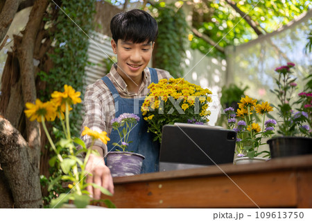A happy and handsome young Asian male florist or gardener is working in a plant nursery in a garden. A happy and handsome young Asian male florist or gardener is working in a plant nursery in a garden. 109613750