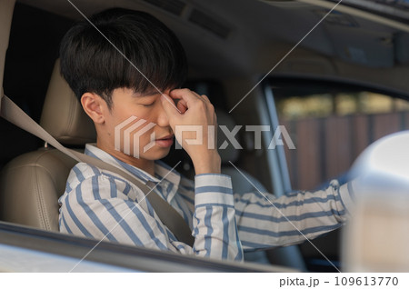 A tired Asian man is suffering from headaches or eye strain while driving a car for long hours. 109613770