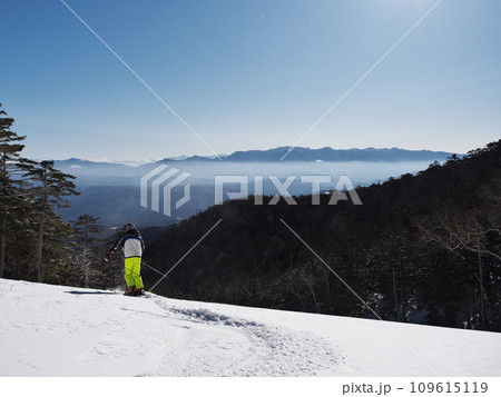 快晴の開田高原マイヤスキー場にて中央アルプスに向って滑走するスキーヤー 109615119