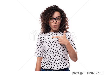 portrait of a young curly brunette well-groomed slender lady dressed in polka dot blouse in black 109617436