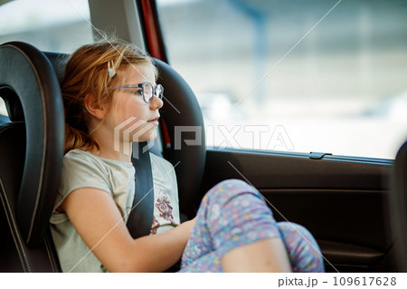 Little Preschool Girl Sitting in Her Car Seat. Happy Child with Eyeglasses looking out of the window. Bored kid on the Way to Family Vacations during Traffic Jam. 109617628