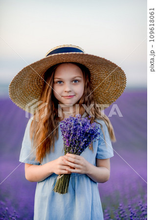 Lavender sunset girl. A laughing girl in a blue dress with flowing hair in a hat walks through a lilac field, holds a bouquet of lavender in her hands. 109618061