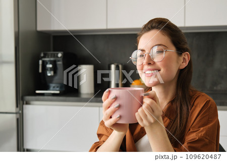 Beautiful young woman, drinking coffee, smiling and looking away with dreamy face, enjoying nice flavour and aroma 109620487