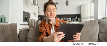 Portrait of young woman looking stressed and tensed at digital tablet, playing difficult level video game, sitting on couch, using gadget, spending time at home Portrait of young woman looking stressed and tensed at digital tablet, playing difficult level video game, sitting on couch, using gadget, spending time at home 109620829