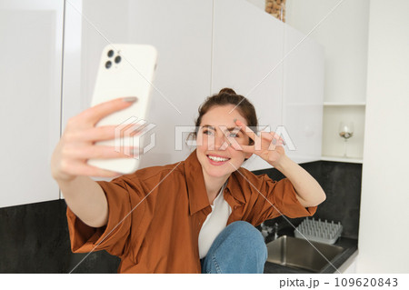 Portrait of beautiful young woman takes selfie on her smartphone, posing for photos, using filter app to take pictures for herself 109620843