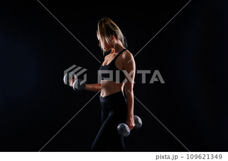 Muscular woman doing exercises with dumbbells at biceps. Photo of strong female isolated on studio Muscular woman doing exercises with dumbbells at biceps. Photo of strong female isolated on studio 109621349