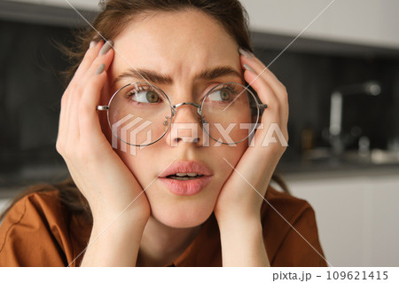 Portrait of woman thinking about something concerning, wearing glasses, touching head, sitting troubled at home Portrait of woman thinking about something concerning, wearing glasses, touching head, sitting troubled at home 109621415