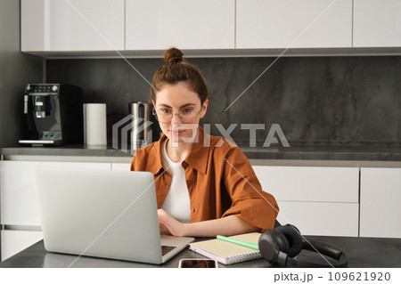 Work and life balance concept. Young woman in glasses, working from home, typing on laptop, student doing homework on computer, sitting in kitchen, freelancing 109621920