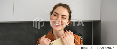 Portrait of young modern woman, 25 years old, standing in the kitchen with notebook, reading notes, student revising for exam Portrait of young modern woman, 25 years old, standing in the kitchen with notebook, reading notes, student revising for exam 109622607