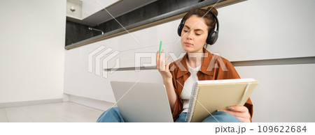 Concentrated young student, woman working on assignment, doing homework on laptop, making notes in notebook during online lesson, remote college course Concentrated young student, woman working on assignment, doing homework on laptop, making notes in notebook during online lesson, remote college course 109622684