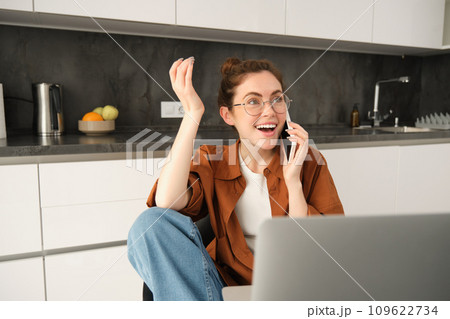 Portrait of young professional, business owner at home, talking on mobile phone, calling coworker while working on remote. Student studying and answer telephone, sitting near laptop 109622734