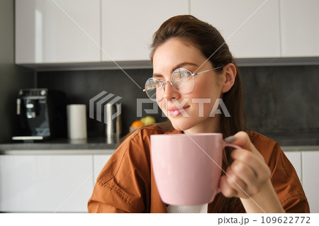Portrait of beautiful brunette woman, sitting in kitchen, taking a break for cup of coffee. Girl drinks tea at home 109622772