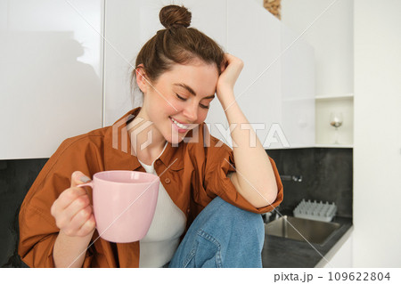 Portrait of beautiful young woman enjoying her morning cup of aromatic coffee, drinking tea while sitting in kitchen and contemplating sunny day Portrait of beautiful young woman enjoying her morning cup of aromatic coffee, drinking tea while sitting in kitchen and contemplating sunny day 109622804