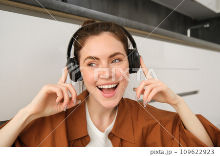 Carefree female model in wireless headphones, listens to music, enjoys favourite tunes in earphones, sings along and smiles Carefree female model in wireless headphones, listens to music, enjoys favourite tunes in earphones, sings along and smiles 109622923