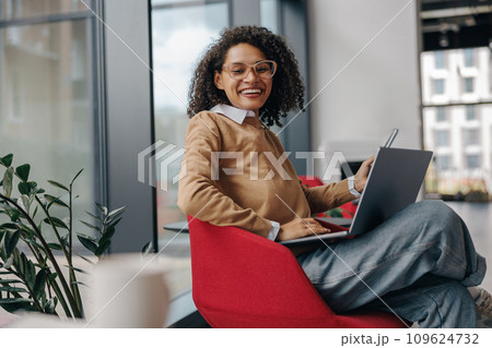 Pretty female freelancer working on laptop while standing on modern coworking background Pretty female freelancer working on laptop while standing on modern coworking background 109624732