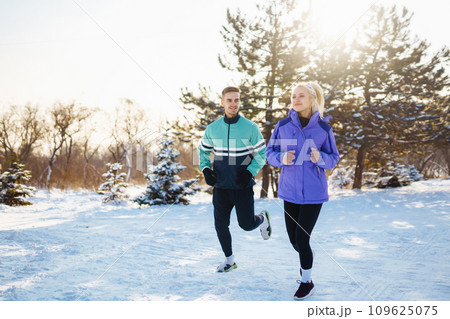 Young couple in sportswear doing morning exercise at snowy forest. Healthy lifestyle concept. Young couple in sportswear doing morning exercise at snowy forest. Healthy lifestyle concept. 109625075