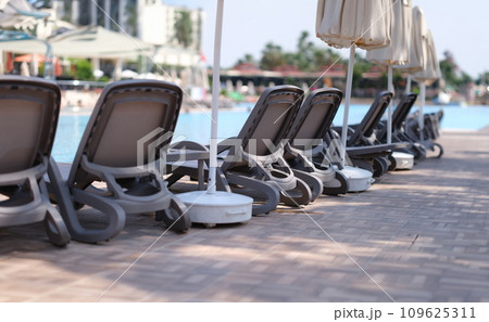 Many empty sun loungers and parasols standing near swimming pool 109625311