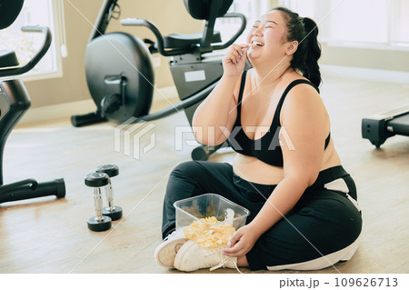 Binge Eating Disorder (BED), happy fat women laugh enjoy unstopable eating chips snack food during relax brake from exercise in fitness sport club. 109626713