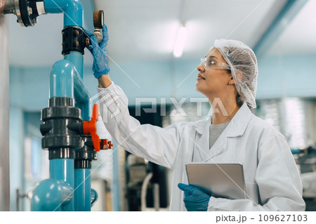 Drinking water factory purification process. Hygiene factory worker female monitor checking valve and water pipe production flow control. Drinking water factory purification process. Hygiene factory worker female monitor checking valve and water pipe production flow control. 109627103