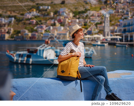 Nice asian Happy Female with backpack Enjoying her holidays on Symi Islands. View of port Symi or Simi, is tiny island of Dodecanese, Greece, calm atmosphere and fabulous architecture. Nice asian Happy Female with backpack Enjoying her holidays on Symi Islands. View of port Symi or Simi, is tiny island of Dodecanese, Greece, calm atmosphere and fabulous architecture. 109629620