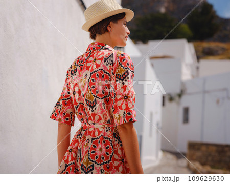 Nice asian Happy Female in boho dress Enjoying Sunny Day on Greek Islands. Travel to Lindos, Mediterranean islands outside tourist season. Tourist woman on vacation in Greece walking through the 109629630