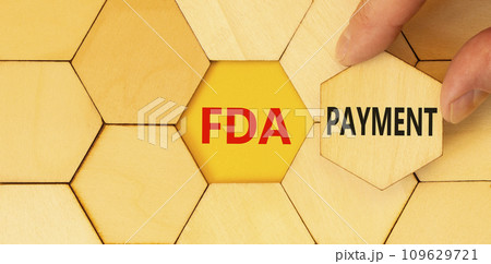 FDA Food and Drug Administration payment symbol. Concept words FDA payment on beautiful wooden puzzle. Beautiful yellow table background. Businessman hand. Business FDA payment concept. Copy space. 109629721