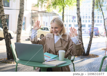 Image of excited blond girl, celebrating, sitting in coffee shop on sunny day, looking at laptop and triumphing 109631077