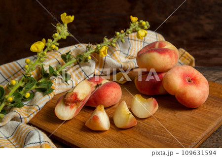 Cutting board with cut and whole saturn peaches or flat peaches on wooden background with yellow kitchen towel.. Cutting board with cut and whole saturn peaches or flat peaches on wooden background with yellow kitchen towel.. 109631594