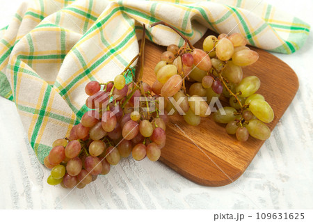 Cutting board with bunch of organic pink grapes on white wooden background.. 109631625