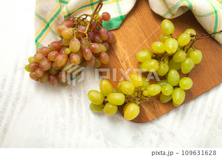Cutting board with bunch of organic green and pink grapes on white wooden background.. 109631628