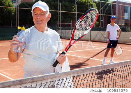Elderly man drinks water on a tennis court 109632076