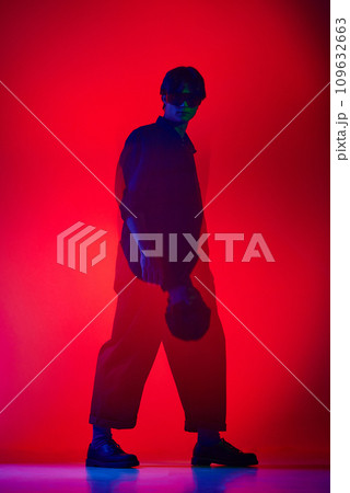 Full-length of handsome, extraordinary young guy in jumpsuit posing over red background in neon light. Fashion show 109632663