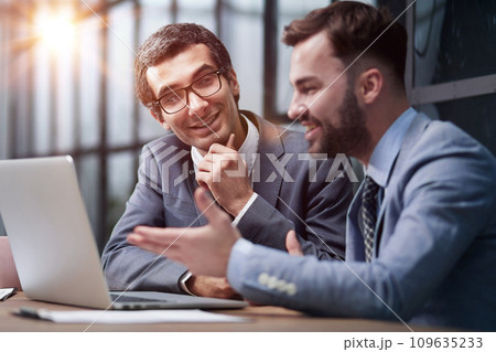 Two young businessmen sitting at workplace and working together in office Two young businessmen sitting at workplace and working together in office 109635233
