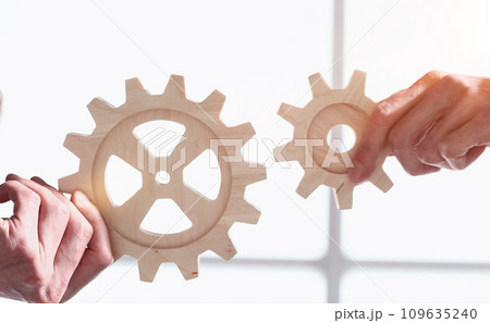 Businessmen in suits connect gears as a symbol of business processes in the company Businessmen in suits connect gears as a symbol of business processes in the company 109635240