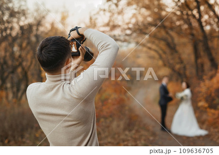 Professional wedding photographer taking pictures of the bride and groom in nature in autumn 109636705