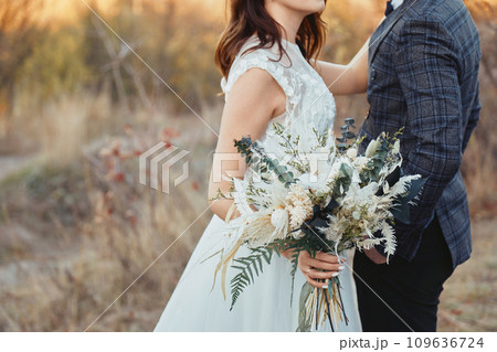 bride and groom holding beautiful bouquet in nature in autumn bride and groom holding beautiful bouquet in nature in autumn 109636724