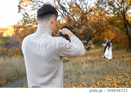 Professional wedding photographer taking pictures of the bride and groom in nature in autumn Professional wedding photographer taking pictures of the bride and groom in nature in autumn 109636725