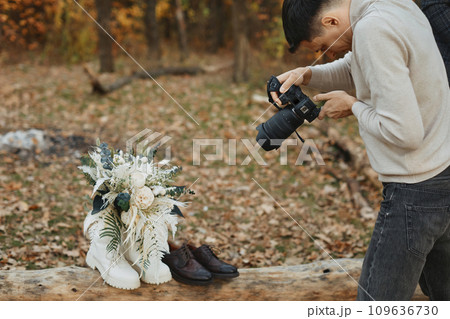 wedding photographer taking pictures of bride and groom shoes, wedding bouquet outdoor. 109636730