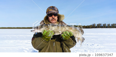 Man Holding a Fish in the Snow. Winter fishing, adventure. Banner, copy space 109637347