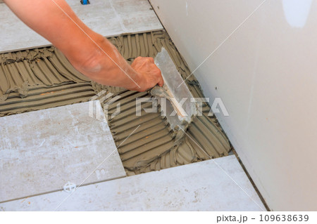 Troweling adhesive onto concrete floor in preparation for laying floor tile. 109638639