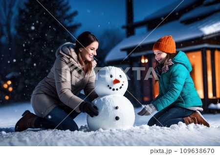 Happy Young Family Making Snowman in the Backyard of their Idyllic House. Mother with her children Puts Snowball together. Family Spending Time Together one Winter Evening. Christmas holiday concept. 109638670